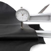 A silver leather gauge is shown next to a piece of black cowhide leather with a lychee texture.