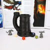 A black emblem dice tower mug is displayed with various polyhedral dice and miniature figures on a white surface.