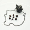 A metal polyhedral dice set with a pendant storage case resting on a white background.