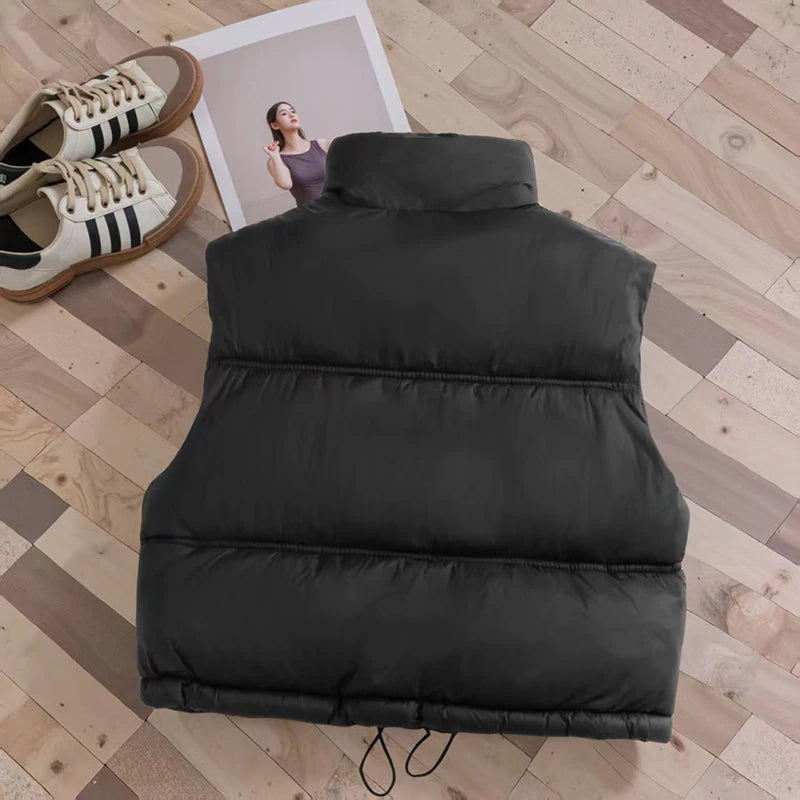 A black padded down vest lying on a wooden floor next to a framed photo.