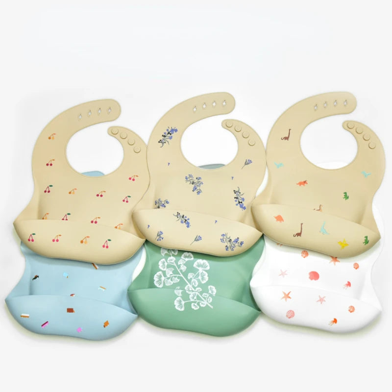 A set of soft silicone waterproof baby bibs with adjustable necks in various pastel colors and floral patterns.
