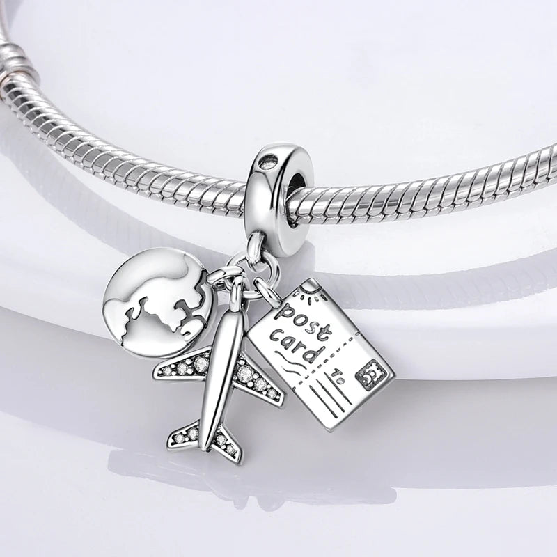 Sterling silver charm beads featuring a globe, an airplane, and a postcard attached to a bracelet chain.
