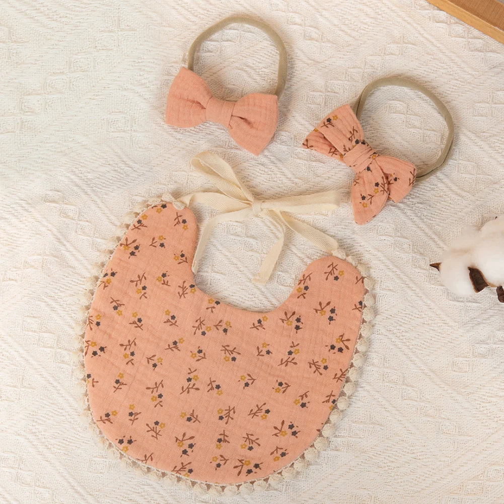 A set of three baby flower bibs and a headband in soft peach fabric with yellow floral embroidery on a white textured backgro