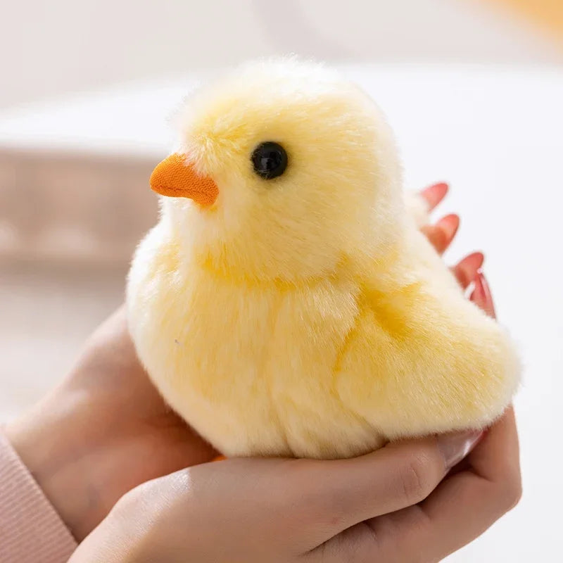 A hand is holding an adorable yellow chick plush toy with orange beak and black eyes.