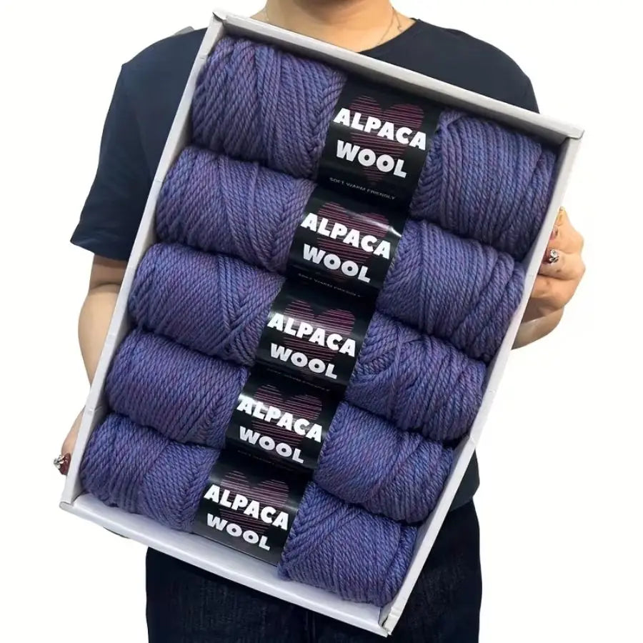 A box containing five skeins of purple alpaca wool yarn for knitting and crochet.