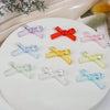 A collection of 12 acrylic bow tie beads in various colors including purple, red, pink, and clear shades arranged on a white 