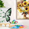 A painting of a yellow sunflower bouquet next to a white butterfly and an acrylic paint palette.