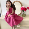 A young girl wearing a pink sleeveless cotton sundress posing in front of a mirror with a floral arrangement.