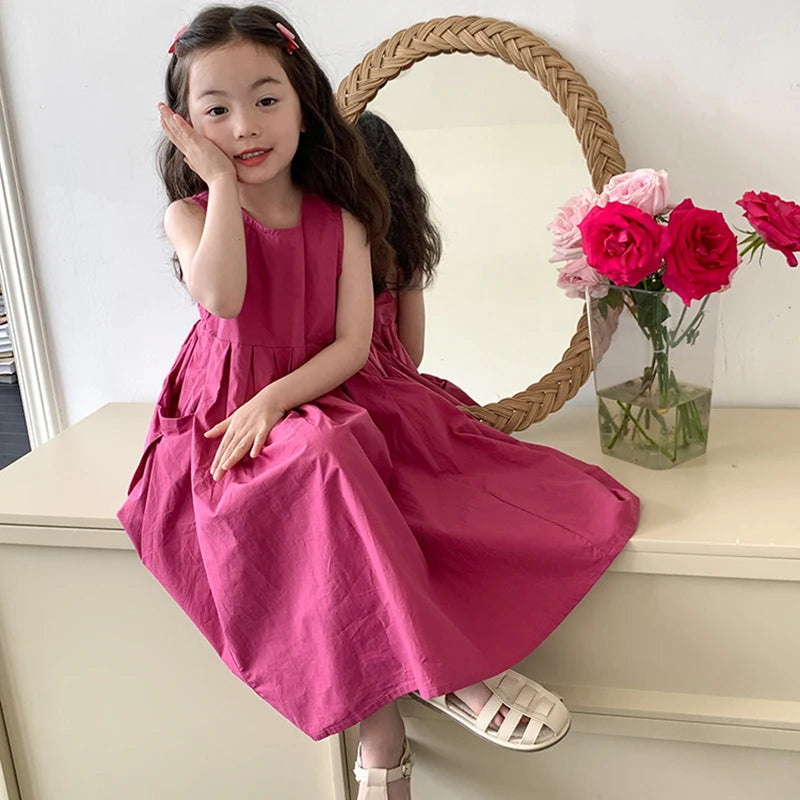 A young girl wearing a pink sleeveless cotton sundress posing in front of a mirror with a floral arrangement.