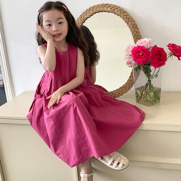 A young girl wearing a pink sleeveless cotton sundress posing in front of a mirror with a floral arrangement.