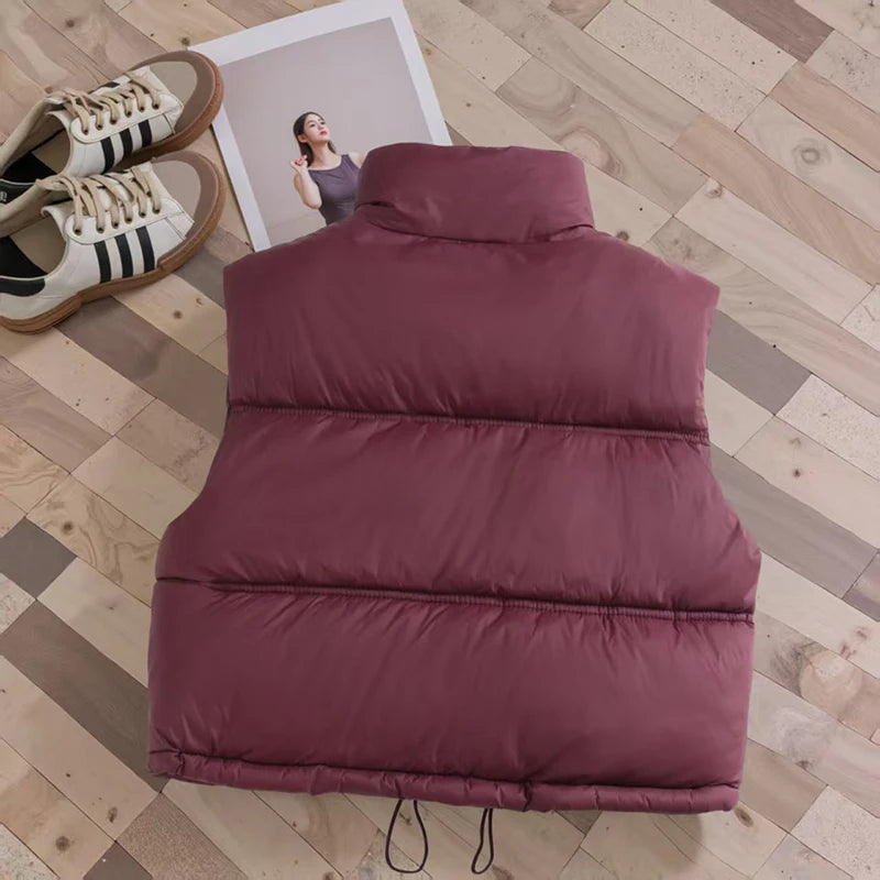 A maroon padded down vest lying on a wooden floor next to a framed photo.