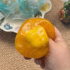 A hand holds a bright orange, squishy stress ball next to translucent blue and yellow glass orbs.