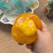 A hand holds a bright orange, squishy stress ball next to translucent blue and yellow glass orbs.