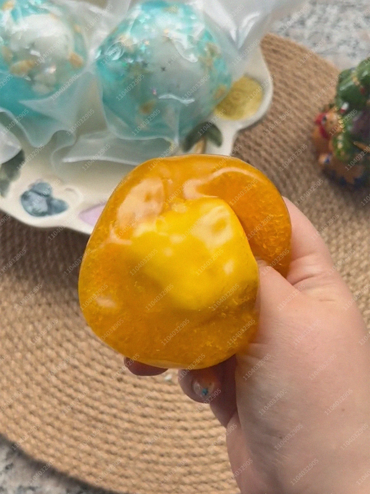 A hand holds a bright orange, squishy stress ball next to translucent blue and yellow glass orbs.
