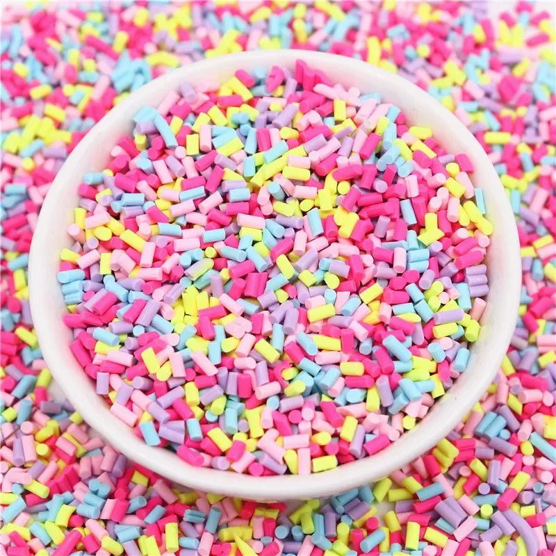 A white bowl filled with colorful polymer clay slice sprinkles for slime and DIY crafts scattered on a pink surface.