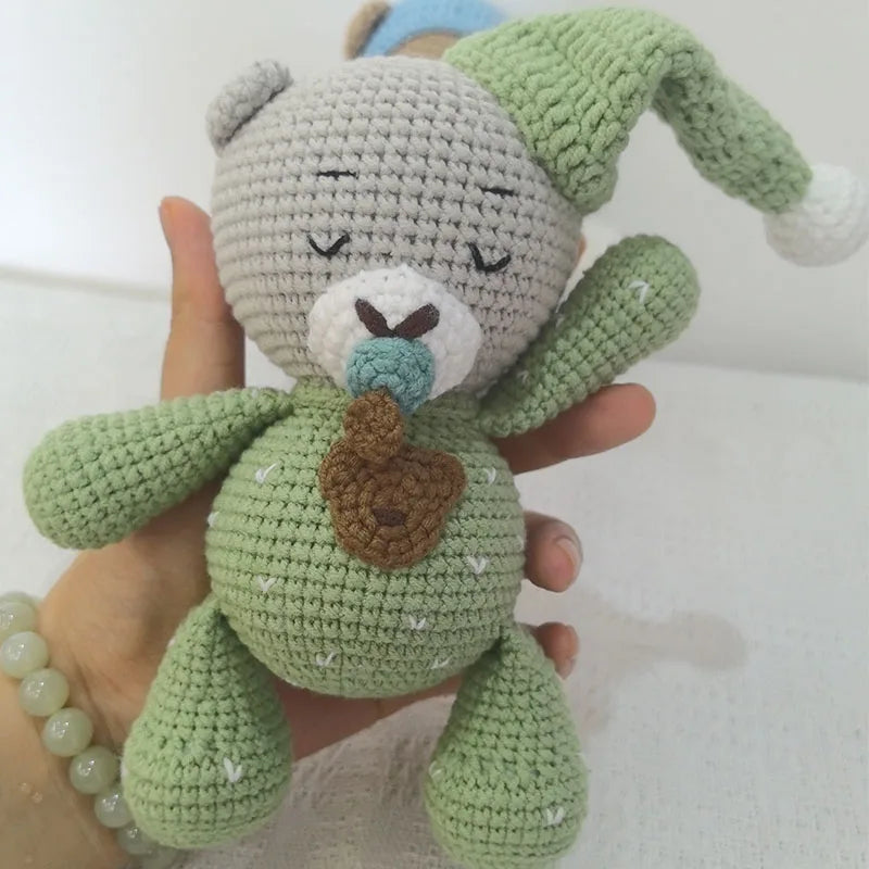 A handmade crochet stuffed bear in light green with white accents is being held by a hand.