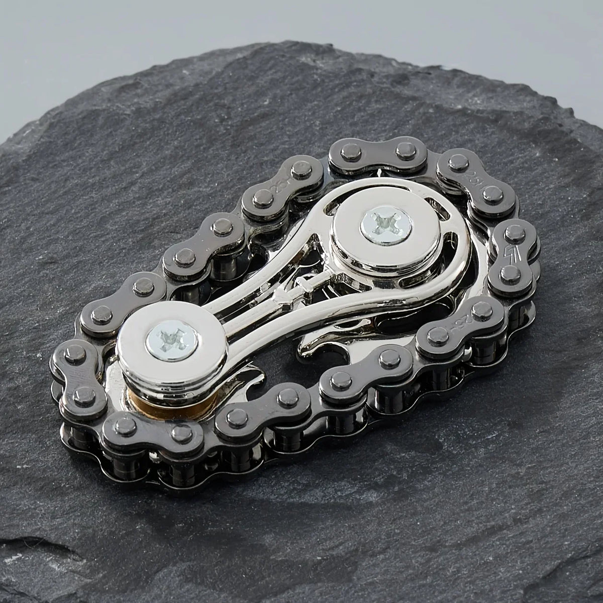 A silver metal fidget spinner with a textured outer ring and a central rotating element resting on a dark stone surface.