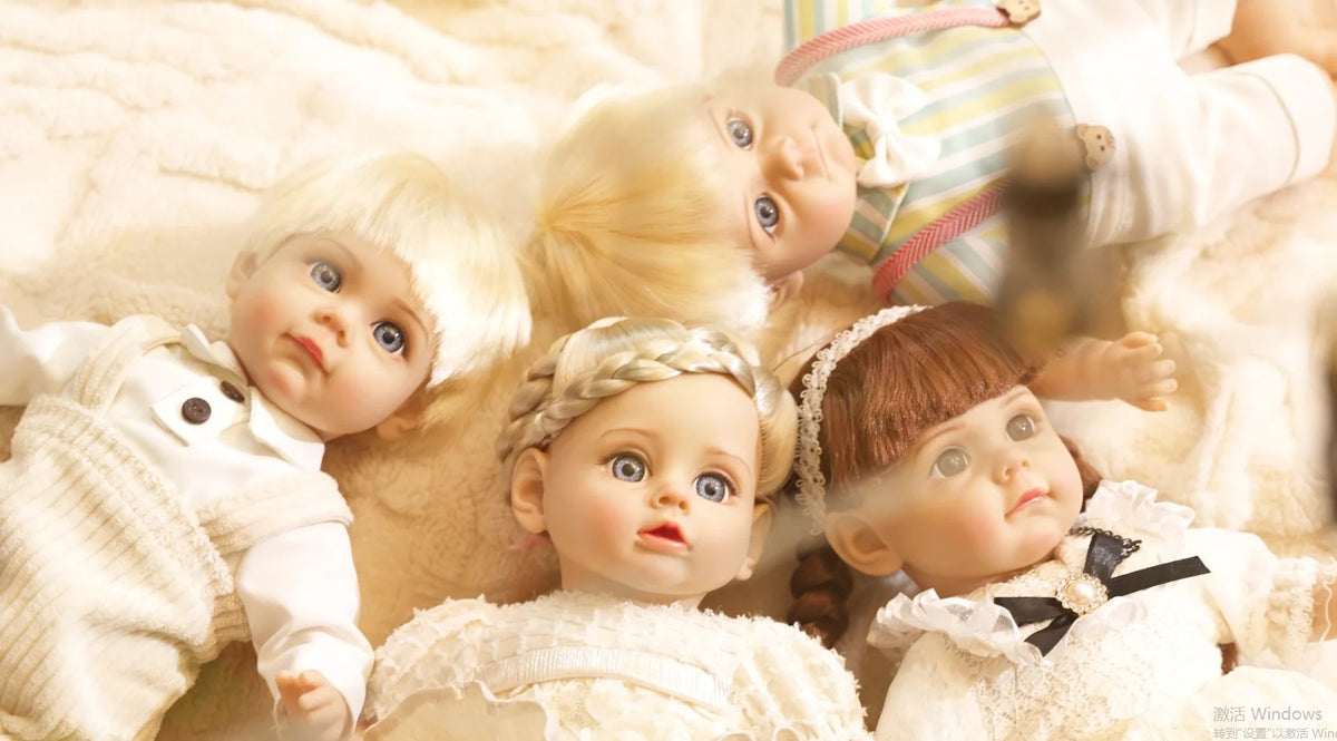 A close-up of a lifelike 14-inch reborn baby doll with blonde hair and a white outfit lying on a soft, light-colored fabric.