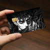 A hand holds a black card featuring an intense anime character design with gold accents.