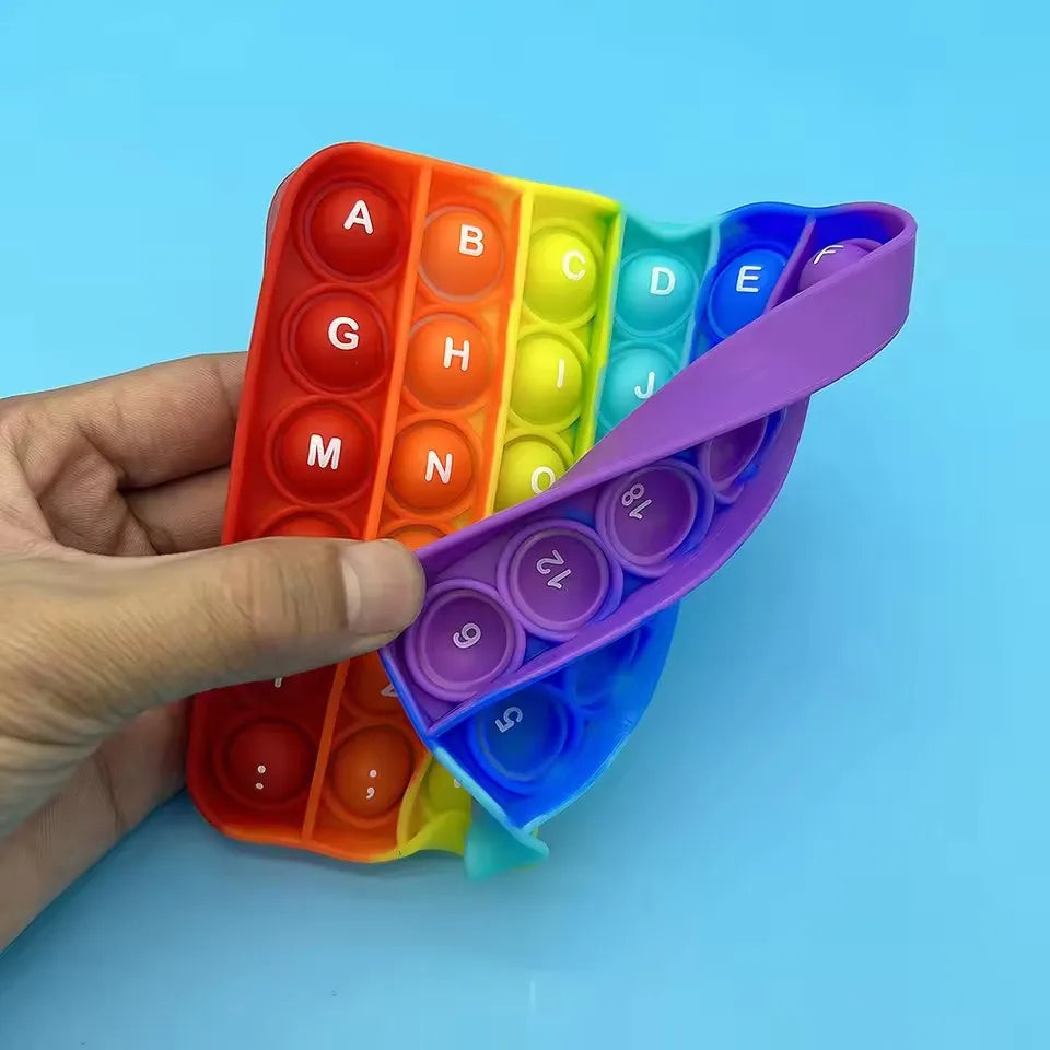 Une main tient un jouet anti-stress 2-en-1 coloré avec des lettres et des chiffres en blocs de silicone poussables.