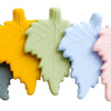 A row of five silicone chew necklaces in pastel colors, including yellow, light green, blue, and pink.