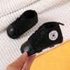 A black canvas first walker for infants is shown resting on a yellow surface.