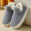 A pair of gray knitted slippers with white faux fur trim resting on a light surface.