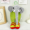 A gray elephant plush toy with green fabric and red feet standing in front of framed papers.