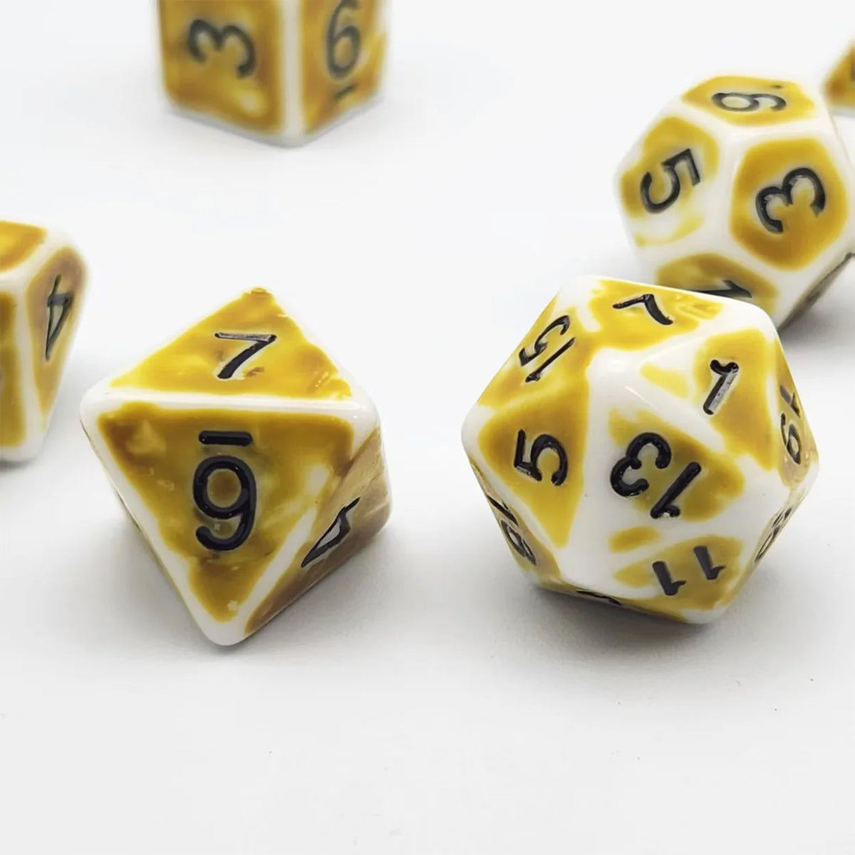 A close-up of several yellow and white polyhedral dice, including a d6, d8, and d10, scattered on a white surface.
