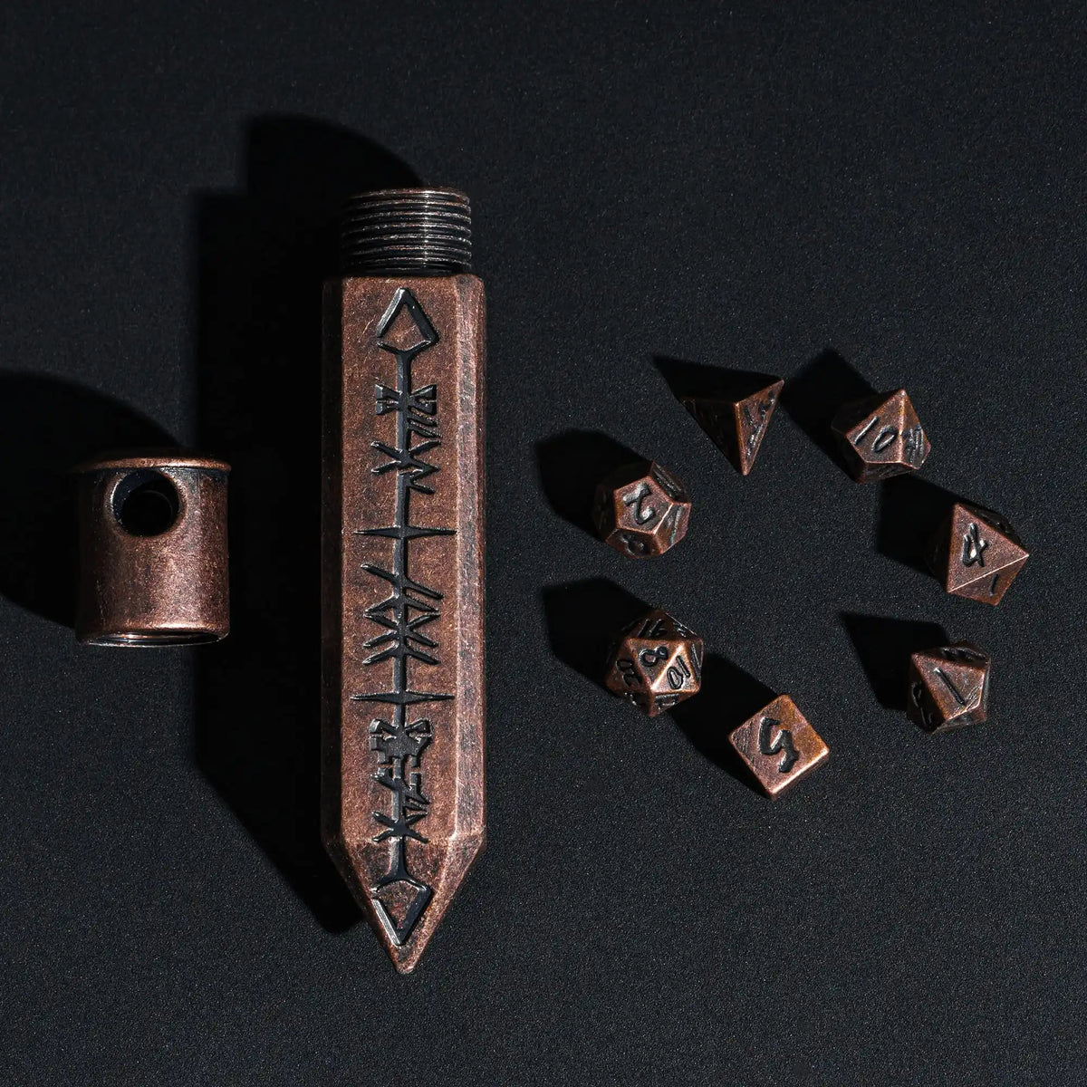 A vertical metal bullet box with a pointed tip and several small metal dice scattered on a dark surface.