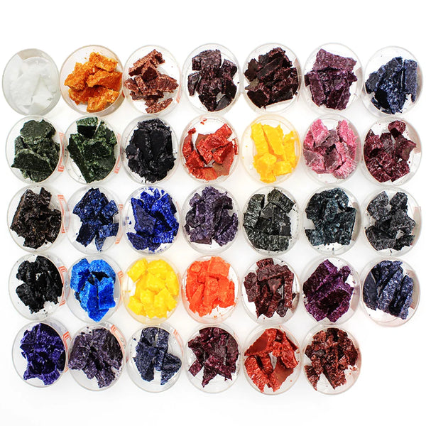 A collection of colorful candle dye chips in various shades including black, purple, blue, yellow, and red.
