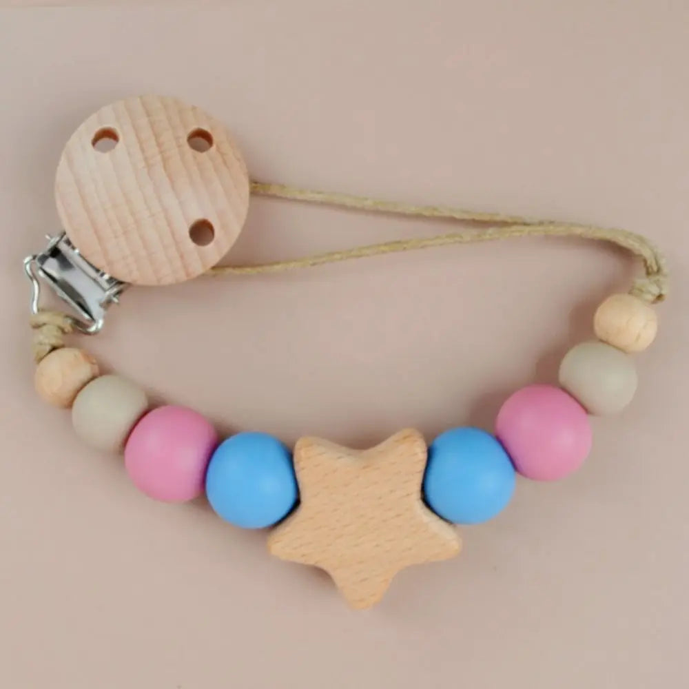 A wooden star shaped pacifier clip with silicone beads and a leather cord on a light pink background.