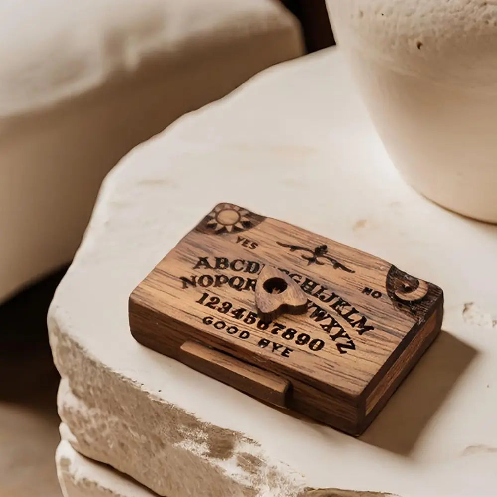 A wooden miniature Ouija board with a drawer resting on a white stone surface.