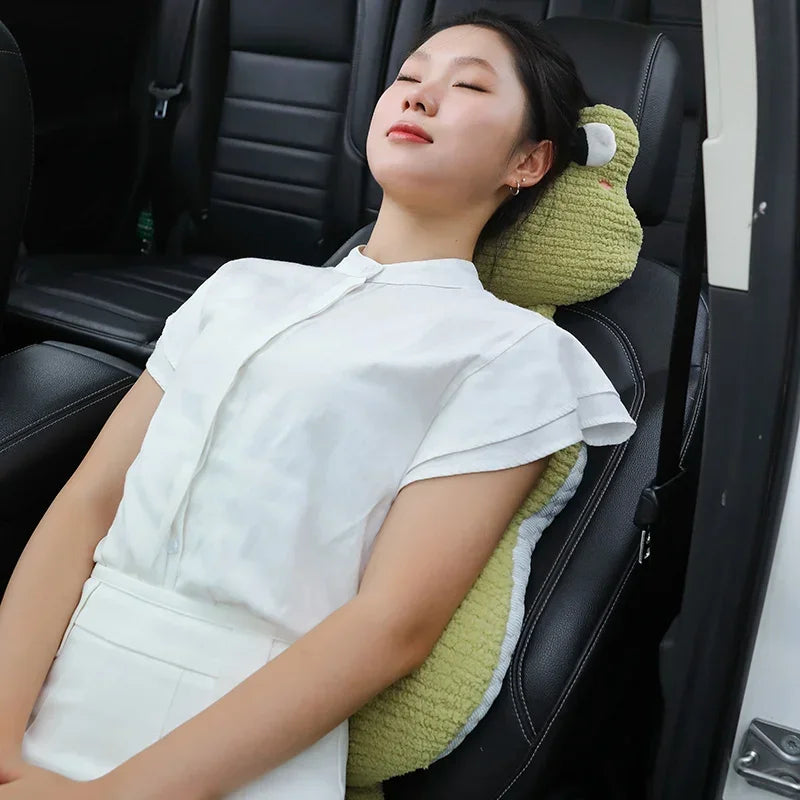 A woman wearing a white shirt is sitting in a black leather seat with a green plush animal lumbar support pillow.