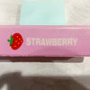 A pink squishy butter stick fidget toy with a strawberry design and the word STRAWBERRY printed on it.