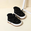 A pair of black baby winter snow boots with plush lining and white soles resting on a light surface.