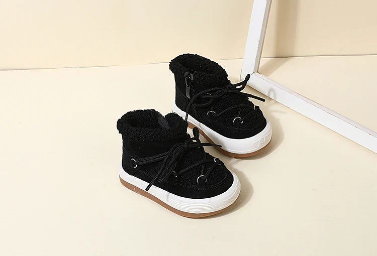 A pair of black baby winter snow boots with plush lining and white soles resting on a light surface.