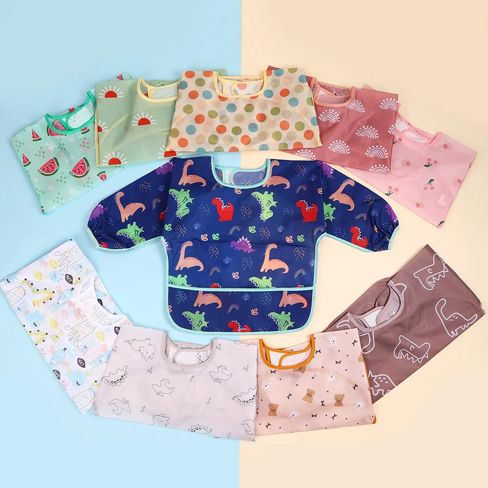 A collection of six colorful waterproof full sleeve baby bibs in various patterns and colors laid out on a light background.