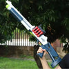 A hand holds a white and blue soft bullet shotgun toy with red shells, set against a green outdoor background.