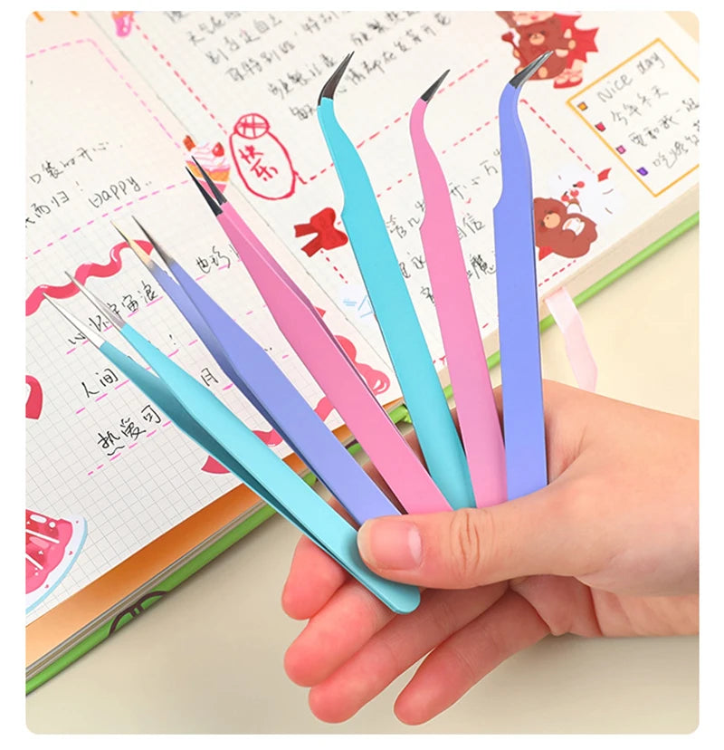 A hand holds several precision stainless steel tweezers in various colors, including pink, blue, and purple, resting on a not