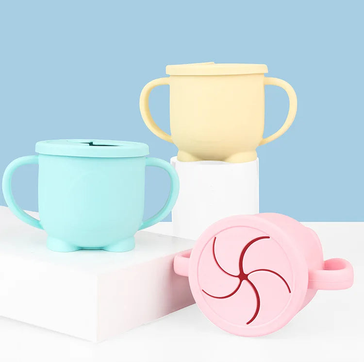 A set of BPA-free silicone snack cups in pale yellow and light blue with lids displayed on a white surface.