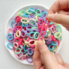 A hand is holding and separating colorful nylon hair ties in various shades of pink, purple, blue, and yellow.