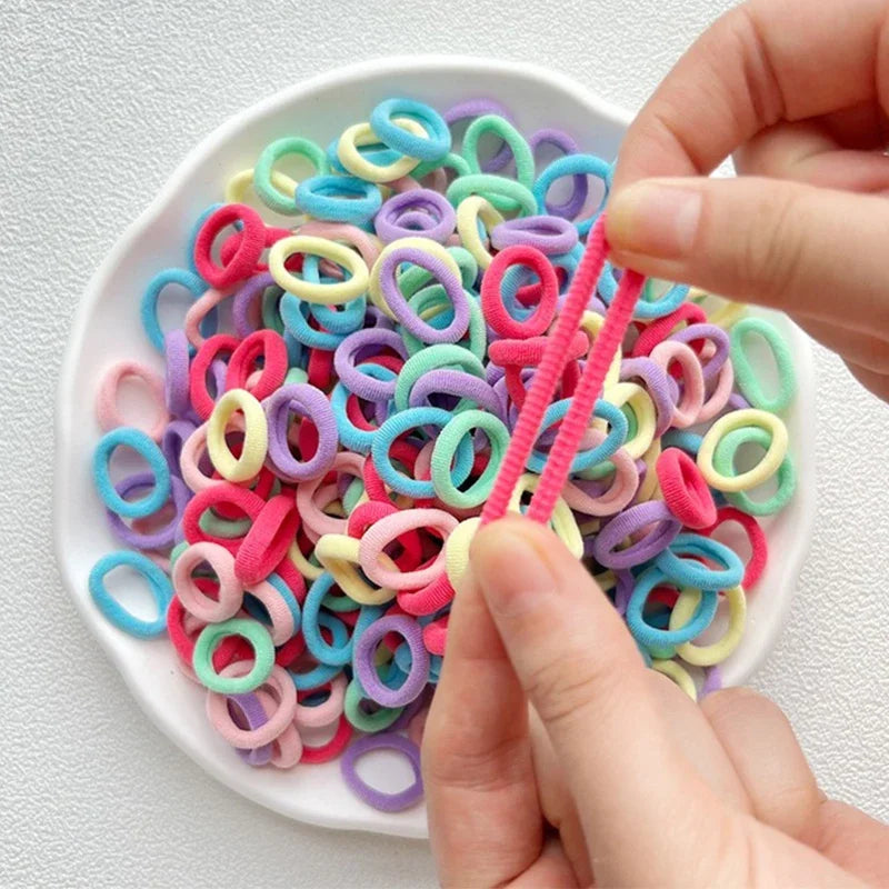 A hand is holding and separating colorful nylon hair ties in various shades of pink, purple, blue, and yellow.