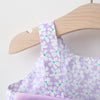 A purple floral baby girl summer dress and sunhat set displayed on a wooden hanger.