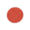 A clear container filled with small, round, reddish-pink glass seed beads for jewelry making.