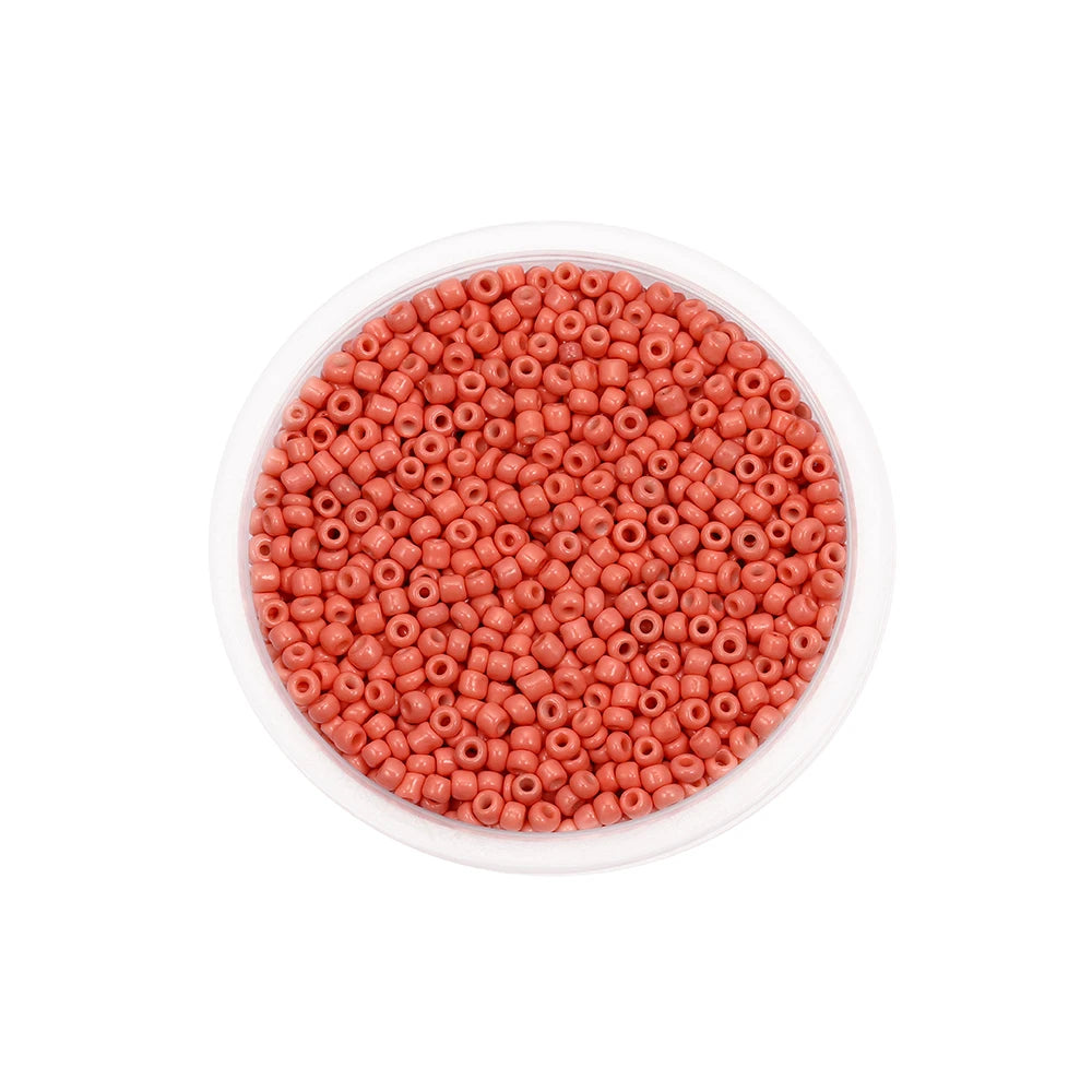 A clear container filled with small, round, reddish-pink glass seed beads for jewelry making.