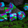 A collection of colorful silicone polyhedral dice resting on green grass and dark rocks.