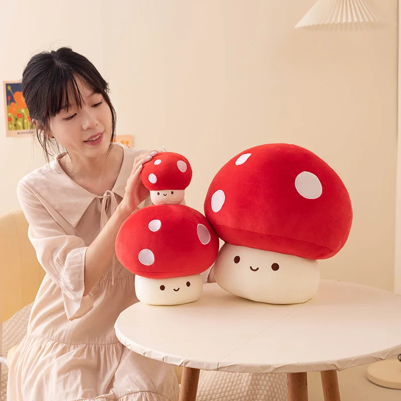 A woman is holding two adorable red mushroom plush pillows on a white table.