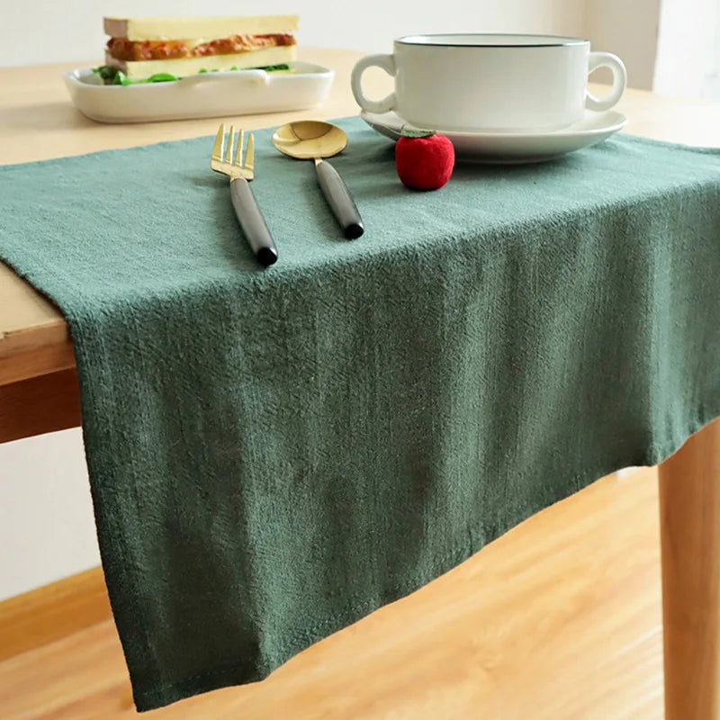 A green linen napkin set is displayed on a wooden table with a sandwich, a cup, and a red apple.