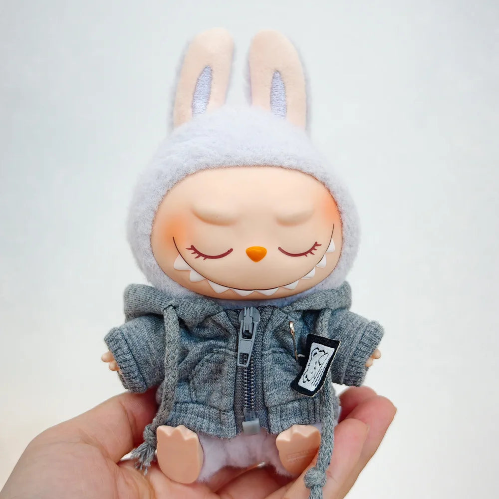 A Labubu doll wearing a gray hoodie and headphones, held in a person's hand.